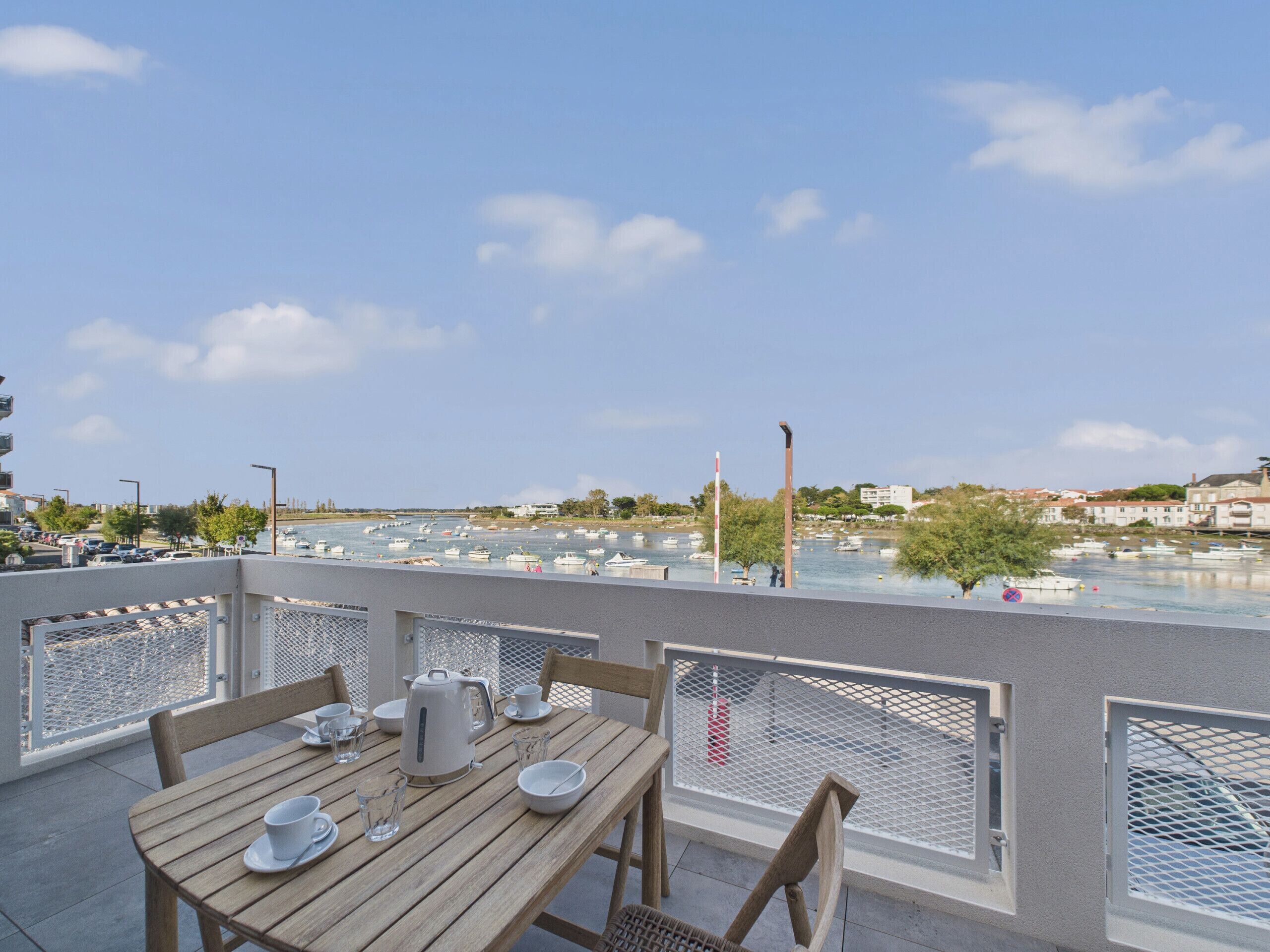 A terrace with a table set for dining, overlooking a marina with boats.