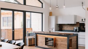 A modern kitchen with a wooden island, pendant lights, and a view to an outdoor deck.