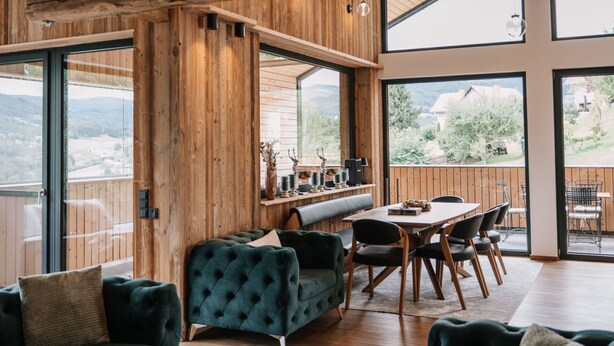 A spacious living area with a wooden interior, a dining table, and a large window overlooking a scenic landscape.