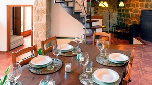 A dining area with a wooden table set for four, surrounded by chairs. A staircase with a metal railing is visible in the background. - Charming barn in the Matarraña, patio with barbecue and AC - Casa de las Letras (Liedo)