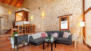 A cozy living room with a stone wall, a gray sofa, a wooden coffee table, and a fireplace. - Charming barn in the Matarraña, patio with barbecue and AC - Casa de las Letras (Liedo)