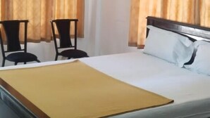 A hotel room with a bed, two chairs, a ceiling fan, and curtains. - Green Mount Residency (Devikolam)