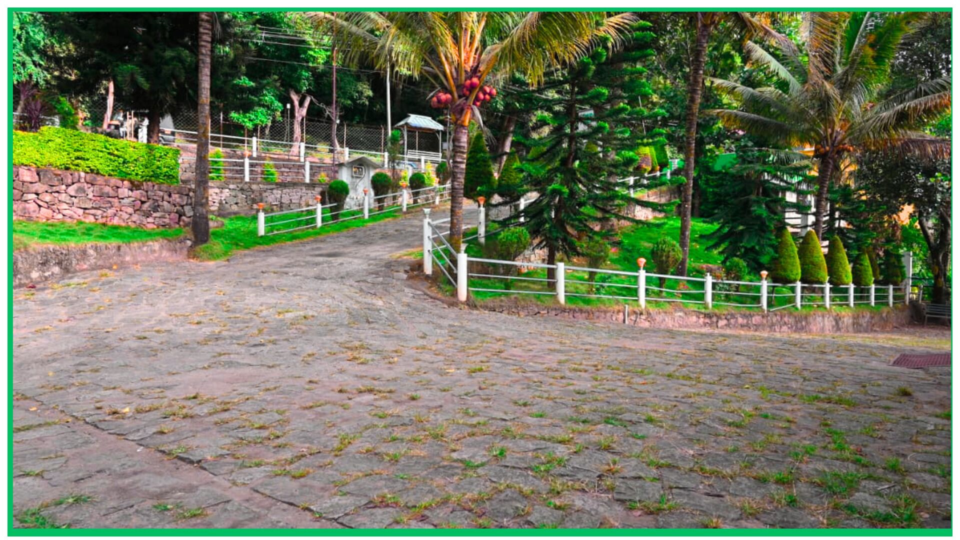 A paved pathway leading up a stone wall with a white fence and greenery on either side.