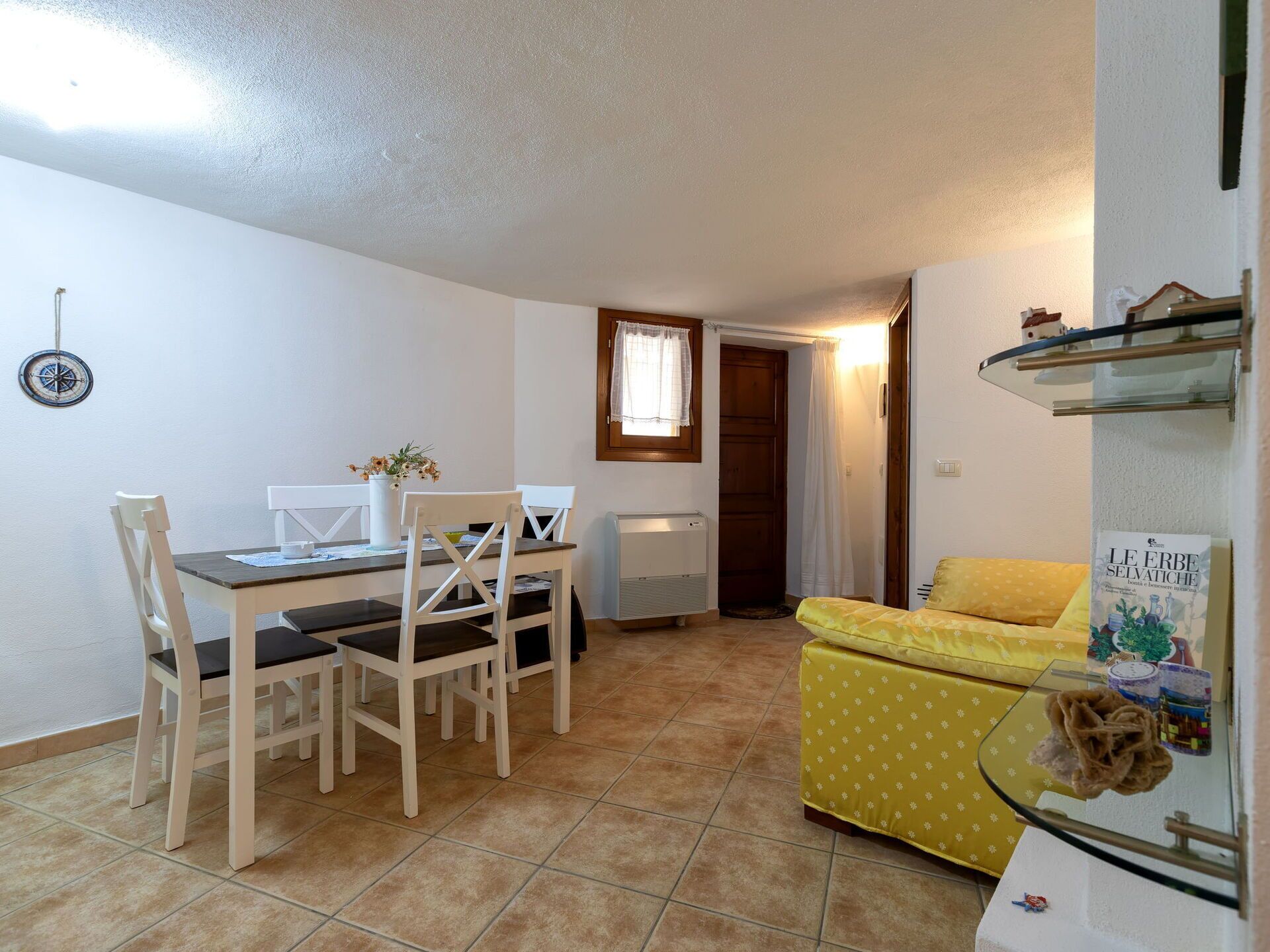 A compact living space with a dining area, a yellow sofa, a small table with chairs, and a radiator.