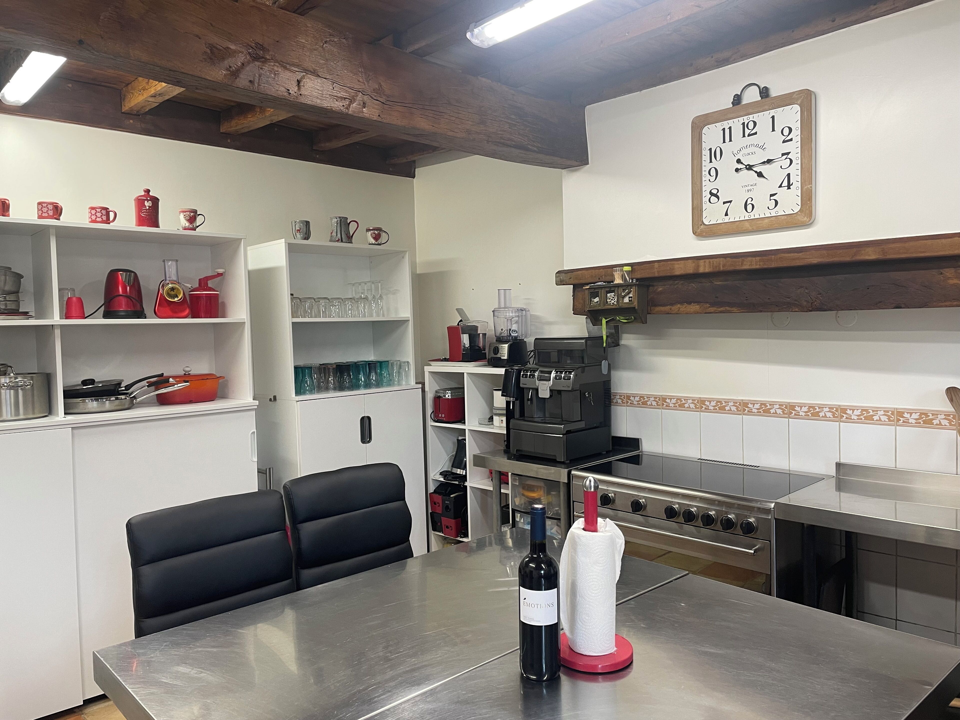 Une cuisine moderne avec des meubles blancs, une machine à café, une bouteille de vin et une horloge au mur.