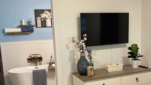 Een moderne badkamer met een badkuip, een wastafel met spiegel en een aan de muur bevestigde televisie.