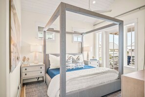 A bedroom with a four-poster bed, a nightstand, a lamp, and a view of the outside.