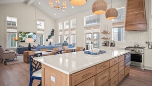 A spacious kitchen with a large island, wooden cabinets, and modern appliances. There is a dining area with blue chairs and a sofa.