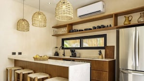A modern kitchen with a central island, wooden stools, hanging wicker lights, and an air conditioning unit. - 2-BD Deluxe Villa 2 Private Pools & Grill (Tulum)