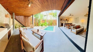A modern outdoor living area with a pool, seating, and a kitchen visible through an open archway. - 2-BD Deluxe Villa 2 Private Pools & Grill (Tulum)