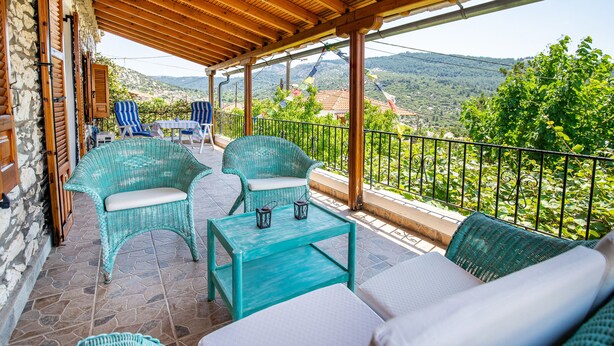 A covered outdoor seating area with wicker furniture and a table, overlooking a scenic landscape.
