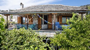 A stone house with a tiled roof, wooden shutters, and a balcony with a chair.