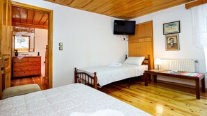 A bedroom with two single beds, a wooden dresser, a television mounted on the wall, and a framed certificate on the wall.