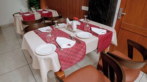 Un espace repas avec des tables préparées pour deux personnes, chacune étant recouverte d’une nappe rouge à motifs, agrémentée d’assiettes blanches et de couverts en argent.