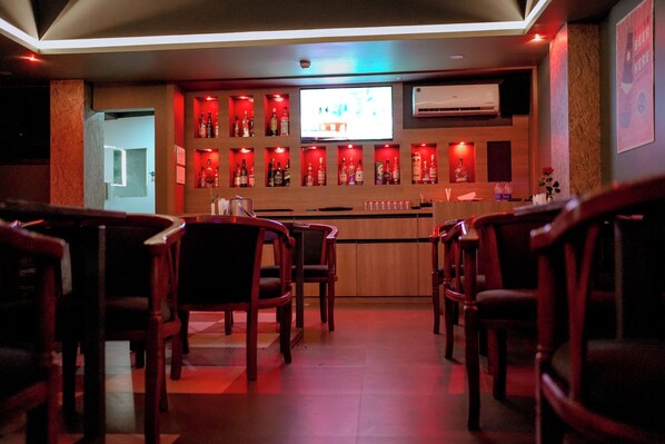 A bar area with wooden chairs, a counter with bottles, and a TV screen.