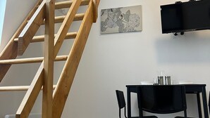 Un escalier en bois menant à l’étage supérieur, une table à manger noire avec des chaises et un téléviseur à écran plat fixé au mur.