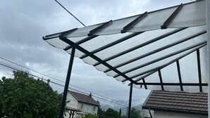 Un quartier résidentiel avec une terrasse couverte, un bâtiment blanc et une voiture garée à l’arrière-plan.