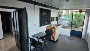 A small room with a tiled floor, a table with two chairs, a sink, and a window with a metal screen.