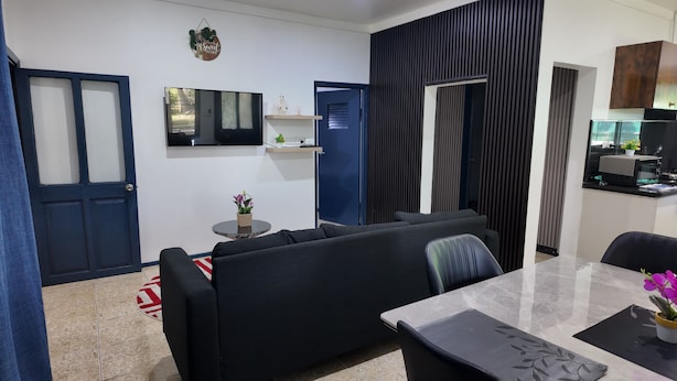 A modern living room with a black sofa, a round coffee table, and a TV mounted on the wall. There is a small plant on the coffee table and a decorative sign above the TV.