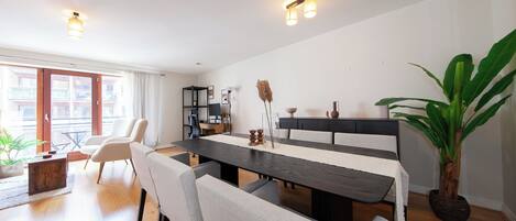 A modern dining area with a long table, white chairs, and a potted plant.