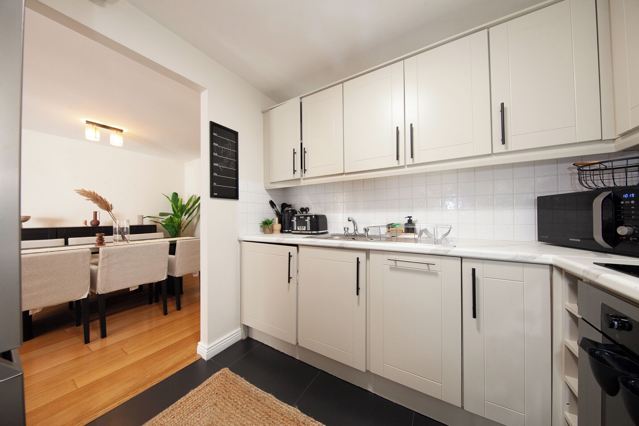 Una cocina moderna con armarios blancos, un microondas negro y una zona de comedor con mesa y sillas.