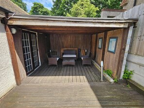 A wooden deck with a covered seating area, a window with bars, and a framed picture on the wall.