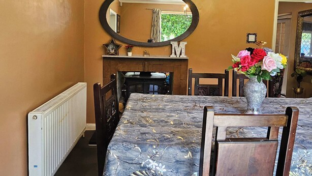 A dining area with a table, chairs, a clock, a fireplace, and a mirror.