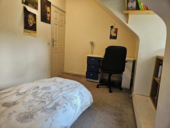 A bedroom with a bed, a desk, a chair, and a bookshelf.