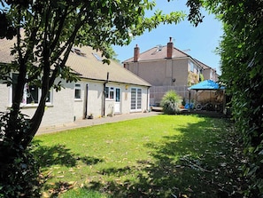 Ein Wohnhaus mit befestigtem Hinterhof, überdachter Terrasse und zweistöckigem Bau mit Ziegeldach.