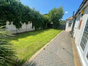 A paved pathway leading to a grassy area with a white fence and greenery.