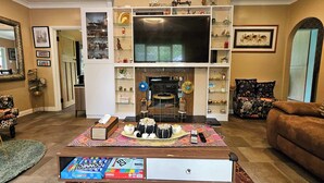 A living room with a large flat-screen TV, a fireplace, a coffee table with board games, and a sofa.
