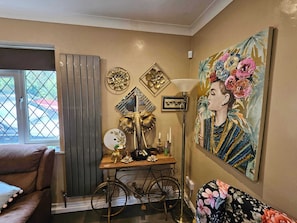 Una habitación con una bicicleta antigua, una mesa decorativa con espejo y un cuadro floral grande en la pared.