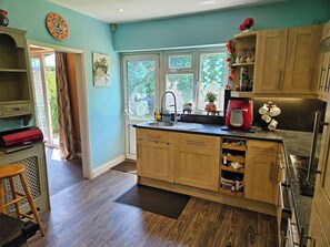 A kitchen with wooden cabinets, a sink, a window with a view of greenery, and a door leading to an outdoor area.