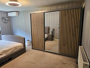 Ein Schlafzimmer mit Bett, Kleiderschrank, Nachttisch und Wandklimaanlage.