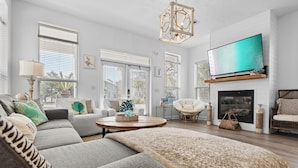 A modern living room with a grey sectional sofa, a round coffee table, a fireplace, and a large flat-screen TV mounted above it.