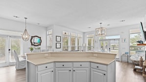A spacious kitchen with white cabinetry, a large island, and a view of the outdoors through large windows.