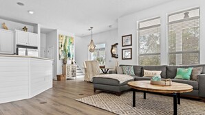 A spacious living area with a grey sofa, a coffee table, and a kitchen with white cabinetry.