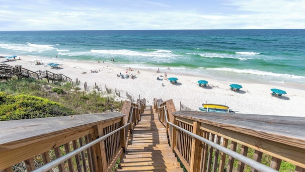 A wooden staircase leading to a beach with umbrellas and people.