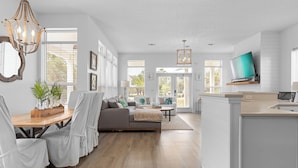 A spacious living area with a wooden dining table, a gray sofa, and a TV mounted on the wall.