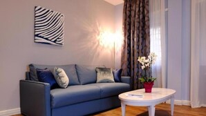 A modern living room with a blue sofa, a white coffee table, and a potted plant. - St Peter SUITES WINTER (Roma)