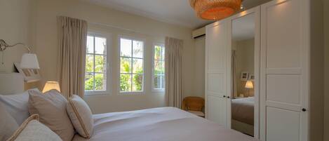 A bedroom with a large bed, two windows with curtains, a wicker lamp, and a wardrobe.