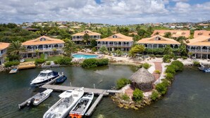 Um resort costeiro com várias villas, uma piscina e barcos atracados no cais.