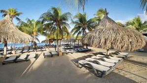 Uma praia com guarda-sóis de palha, cadeiras de espreguiçadeira e palmeiras.