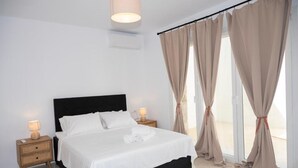 A neatly made bed with white linens, a black headboard, and two bedside tables with lamps. - Adyton Luxury Suite Mykonos Exclusive Pool Oasis (Mykonos)