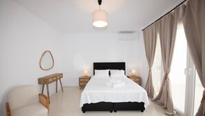 A modern bedroom with a large bed, bedside lamps, a wooden nightstand, a chair, and a hanging light fixture. - Adyton Luxury Suite Mykonos Exclusive Pool Oasis (Mykonos)