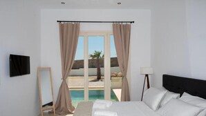 A bedroom with a bed, a TV, a lamp, and a view of a pool and beach. - Adyton Luxury Suites Mykonos Private Pool Getaway (Mykonos)