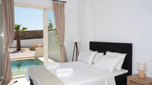 A hotel room with a bed, a bedside lamp, and a view of a pool and outdoor area. - Adyton Luxury Suites Mykonos Private Pool Getaway (Mykonos)