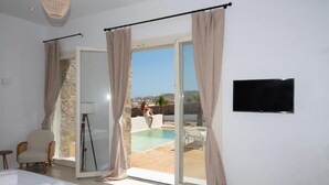 A bedroom with a bed, a chair, a TV, and a sliding glass door leading to a pool area. - Adyton Luxury Suites Mykonos Private Pool Getaway (Mykonos)