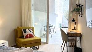Une chambre moderne avec un lit, un fauteuil jaune, un bureau avec une chaise et une porte-fenêtre coulissante donnant sur un espace extérieur.