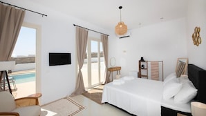 Un dormitorio con cama, televisión, mesita de noche, lámpara y vista a la piscina.